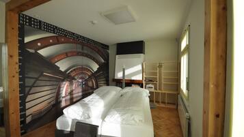Quarto com cama, radiador, prateleira e parede com desenho circular.