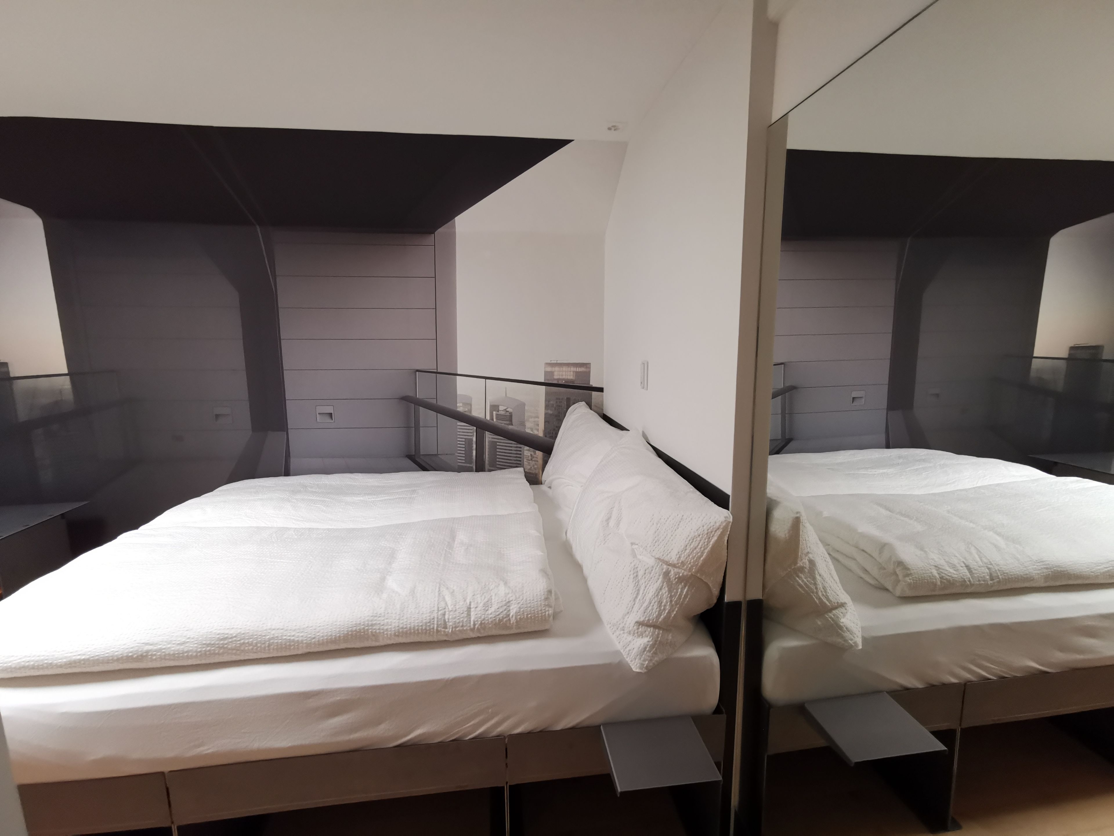 A modern hotel room with a large bed, a small bedside table, and a mirror reflecting the room.