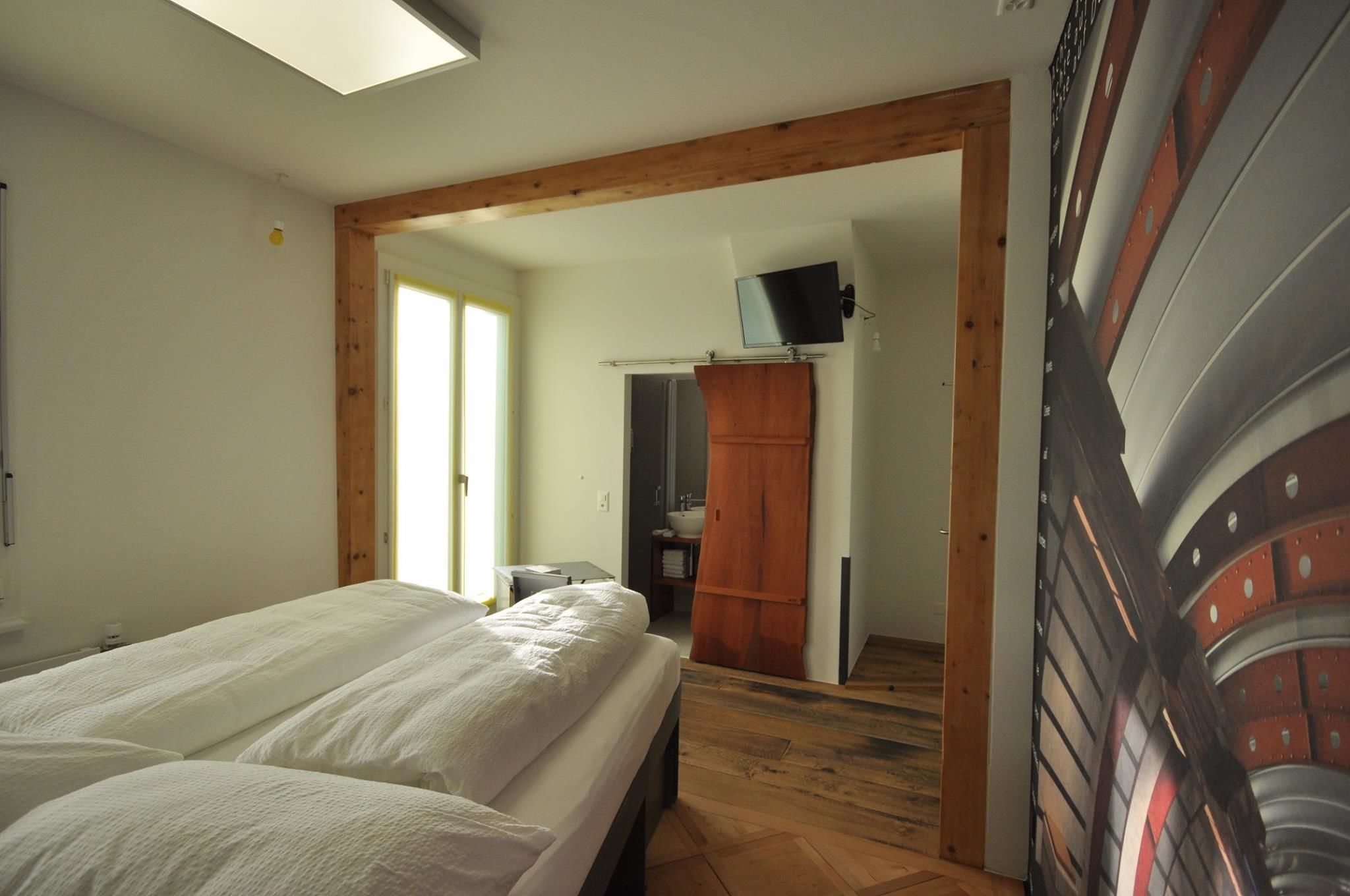 Une chambre avec deux lits, des poutres en bois, une télévision et une salle de bain visible à travers une porte ouverte.