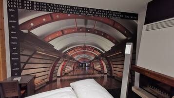 Quarto com um mural de um túnel, cama com roupa de cama branca e um banco de madeira.