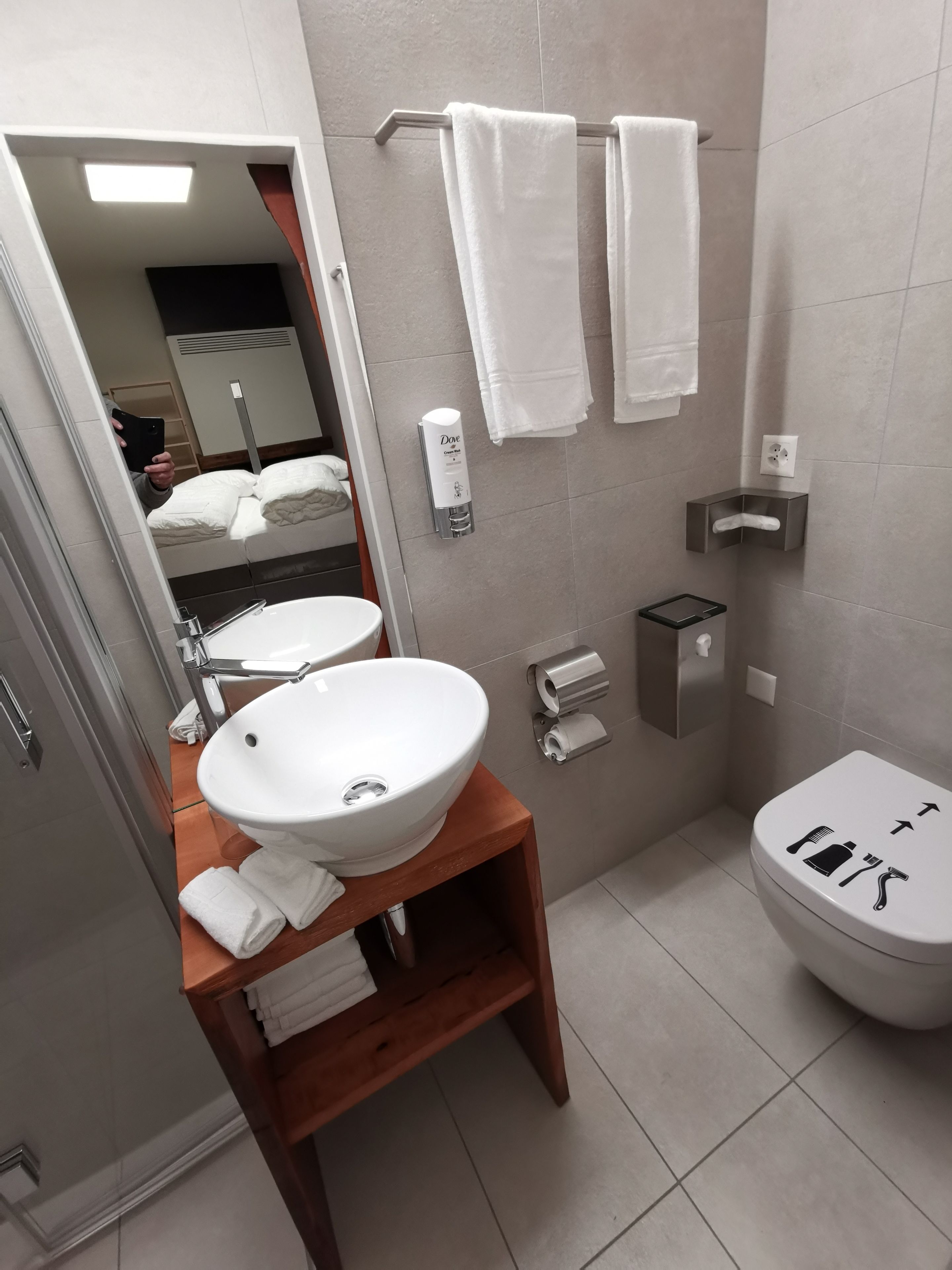 Een moderne badkamer met een houten wastafel, een witte wasbak, een spiegel en een toilet met pictogrammen op de deksel.