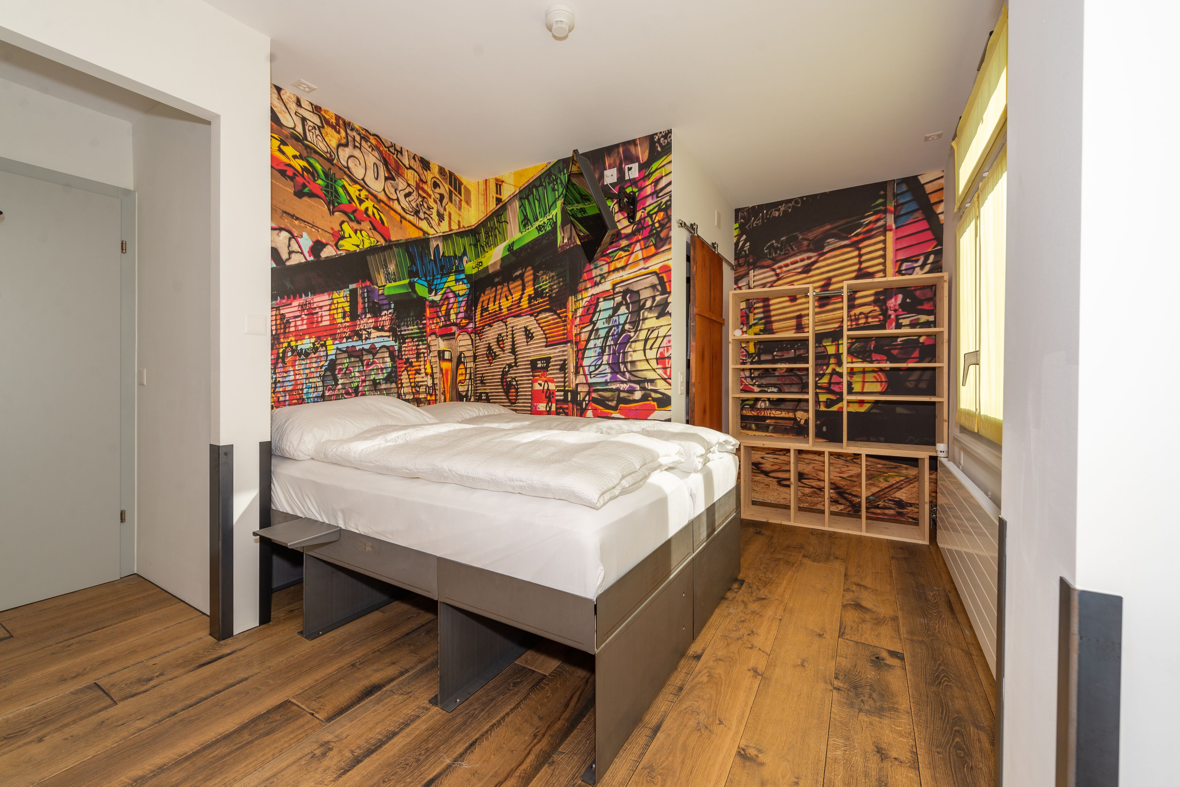 Ein Schlafzimmer mit einem Bett, Holzboden, einer farbenfrohen Graffiti-Wand und einer eingebauten Bücherwand.
