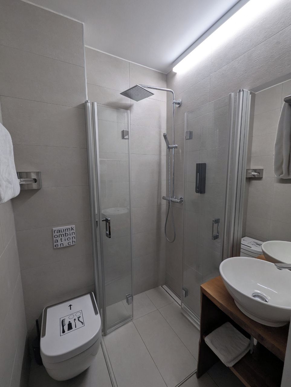 Un baño moderno con ducha envuelta en vidrio, inodoro y secamanos, y lavabo con espejo.