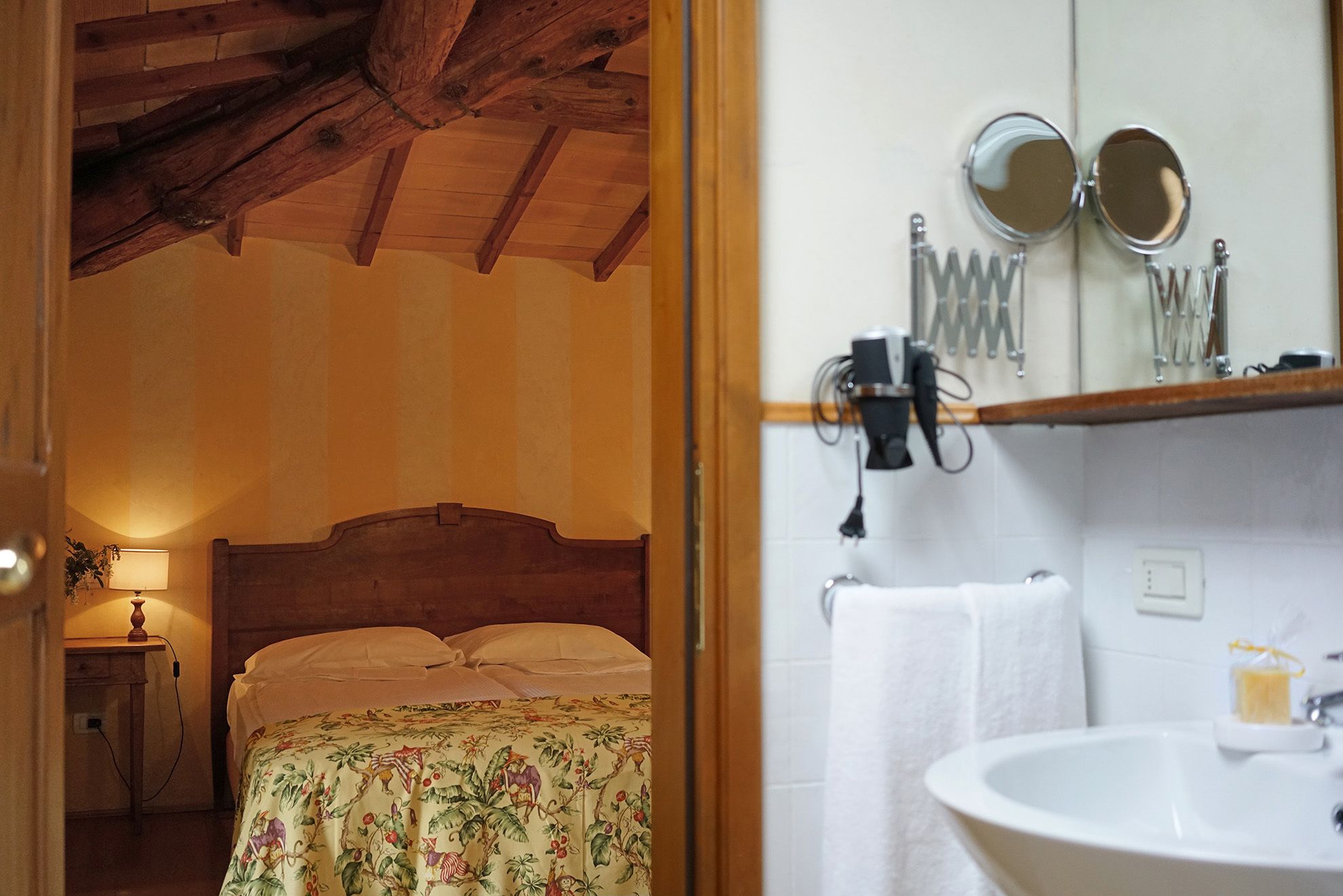 A bedroom with a wooden ceiling, a bed with floral bedding, and a nightstand with a lamp.