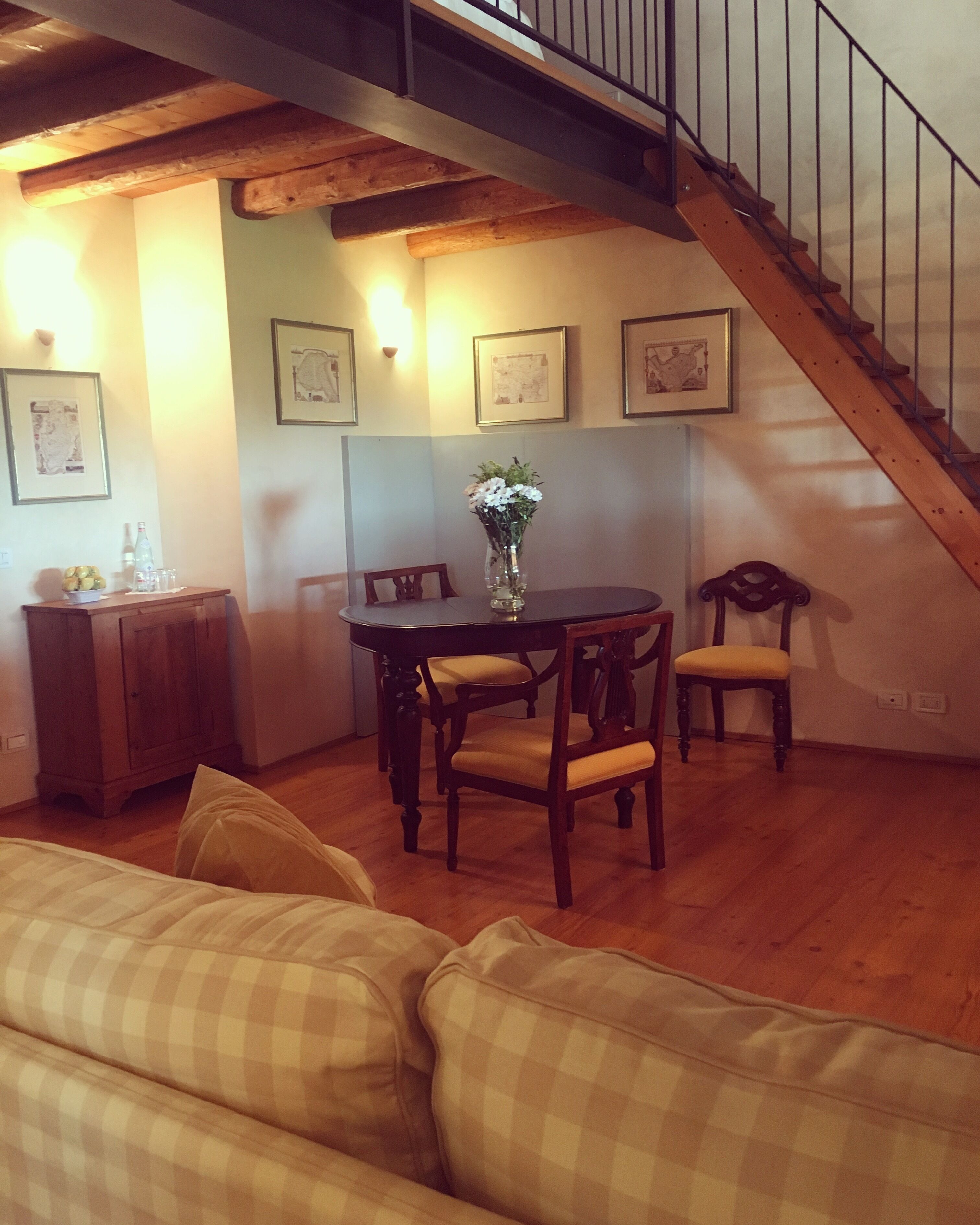 Un comedor con una mesa y sillas de madera, un jarrón con flores y una escalera que sube a un nivel superior.