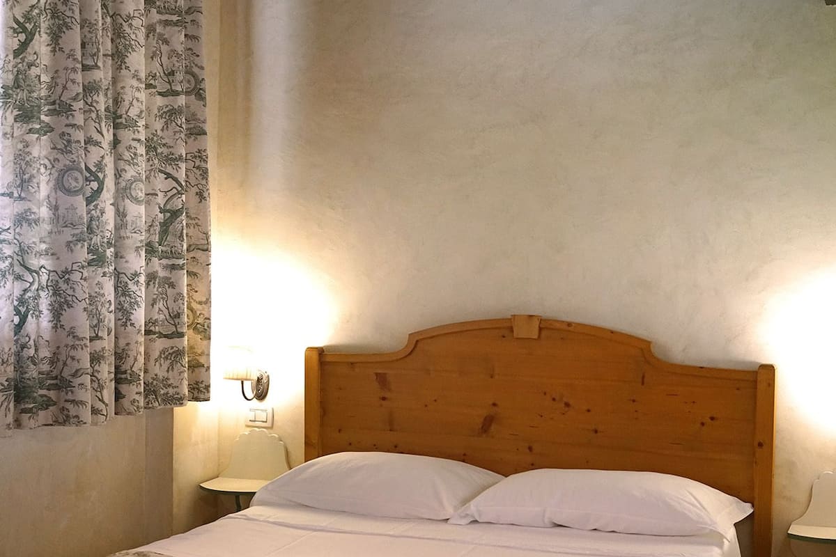 A bedroom with a wooden bed, white bedding, a bench, and a nightstand with a lamp.