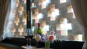 A window with a brick pattern, a wine bottle, two wine glasses, and a vase with flowers on a wooden surface. - Domus Cariana (San Pietro in Cariano)