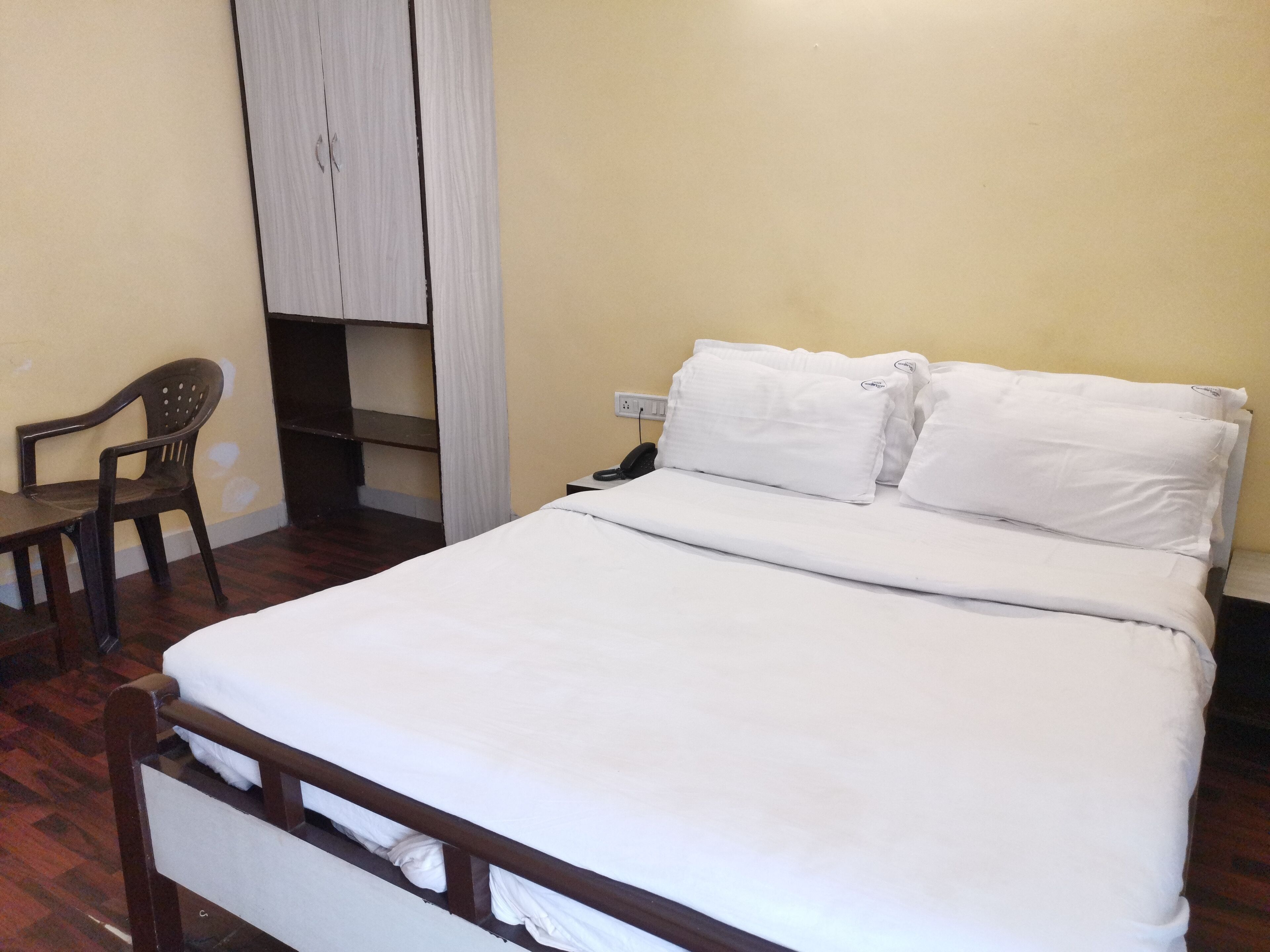 A neatly made bed with white bedding, a wooden headboard, and a small desk with a chair.