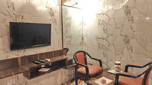 A modern hotel room with a marble wall, a flat-screen TV, a wooden console table, two upholstered chairs, and a coffee maker. - The Blue Lagoon Resort (Mawal)