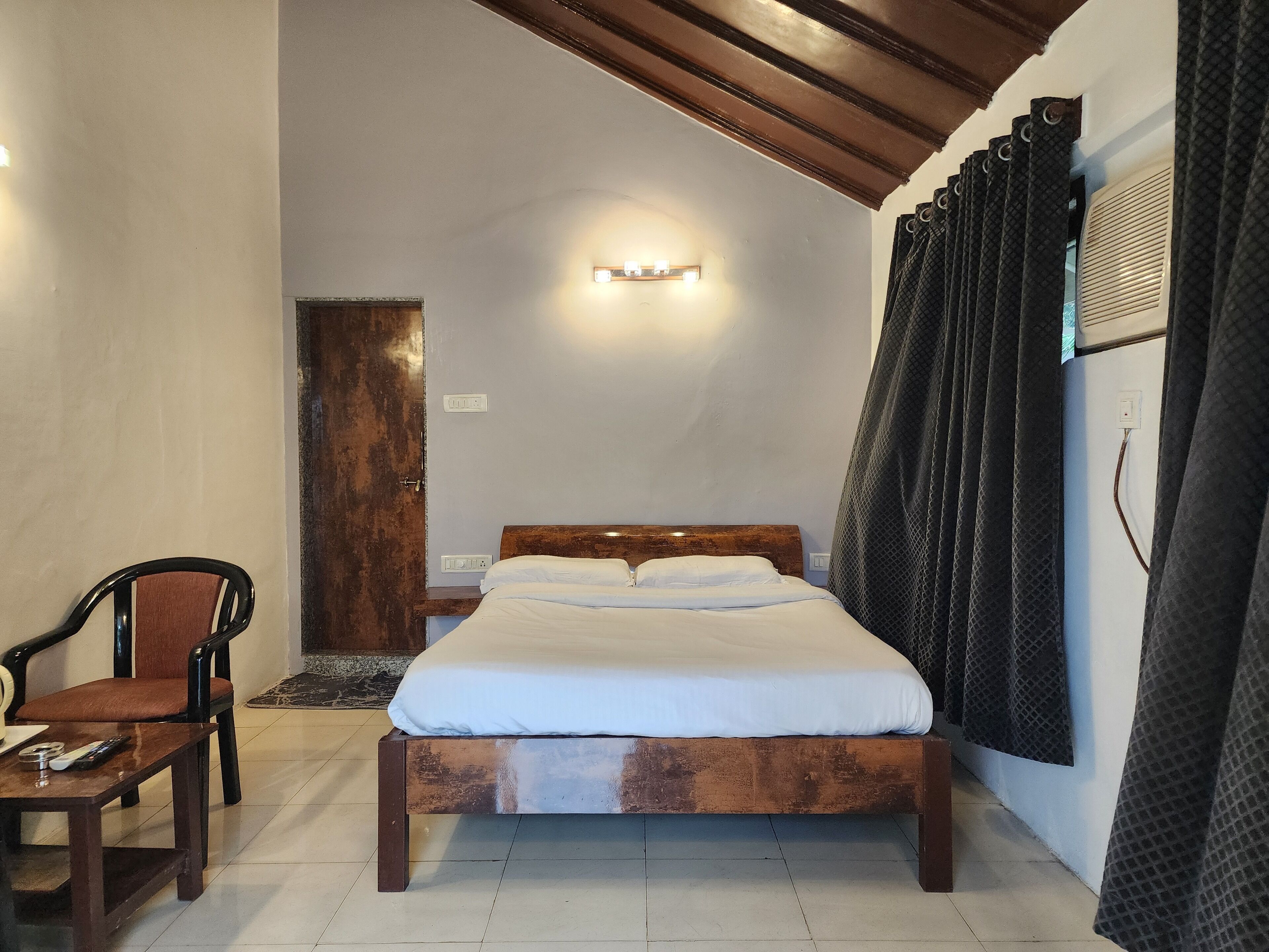 A bedroom with a wooden bed, a chair, a nightstand, and a wall-mounted light.