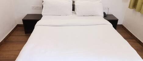 Una cama bien tendida con ropa blanca, dos mesitas de noche y un cabecero marrón.