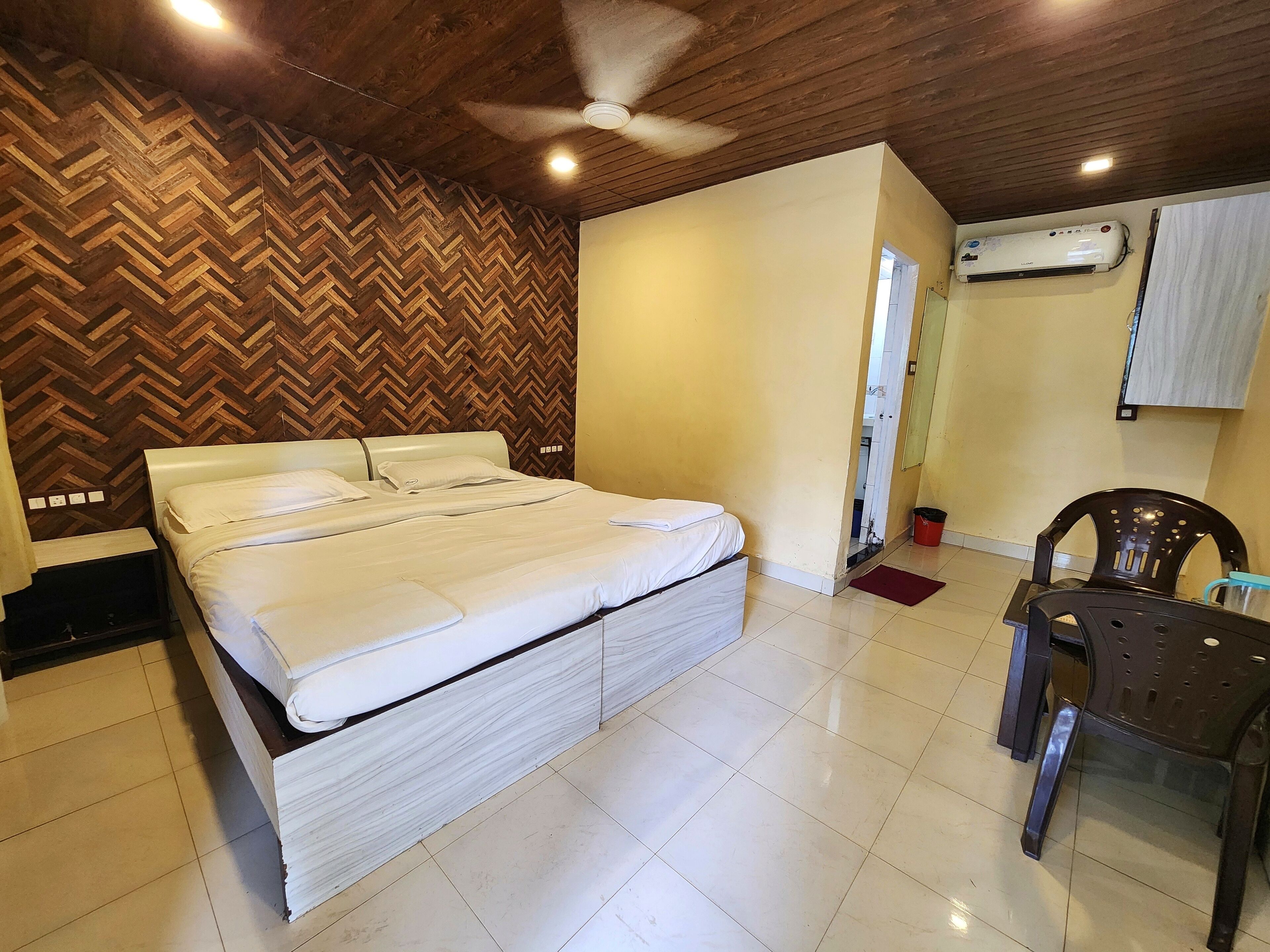 A bedroom with a bed, a ceiling fan, an air conditioning unit, and a chair.