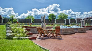 Un patio con mesa y sillas, rodeado por un jardín con flores y vistas a montañas.
