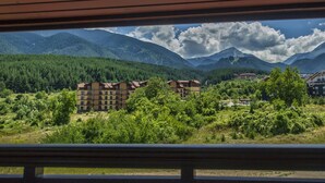 Vista de un paisaje montañoso con un edificio de varios pisos y techo plano, rodeado de vegetación y árboles.