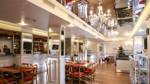 Un comedor espacioso con techo alto y candelabros, una zona de bar con una variedad de botellas, y un árbol de Navidad al fondo.