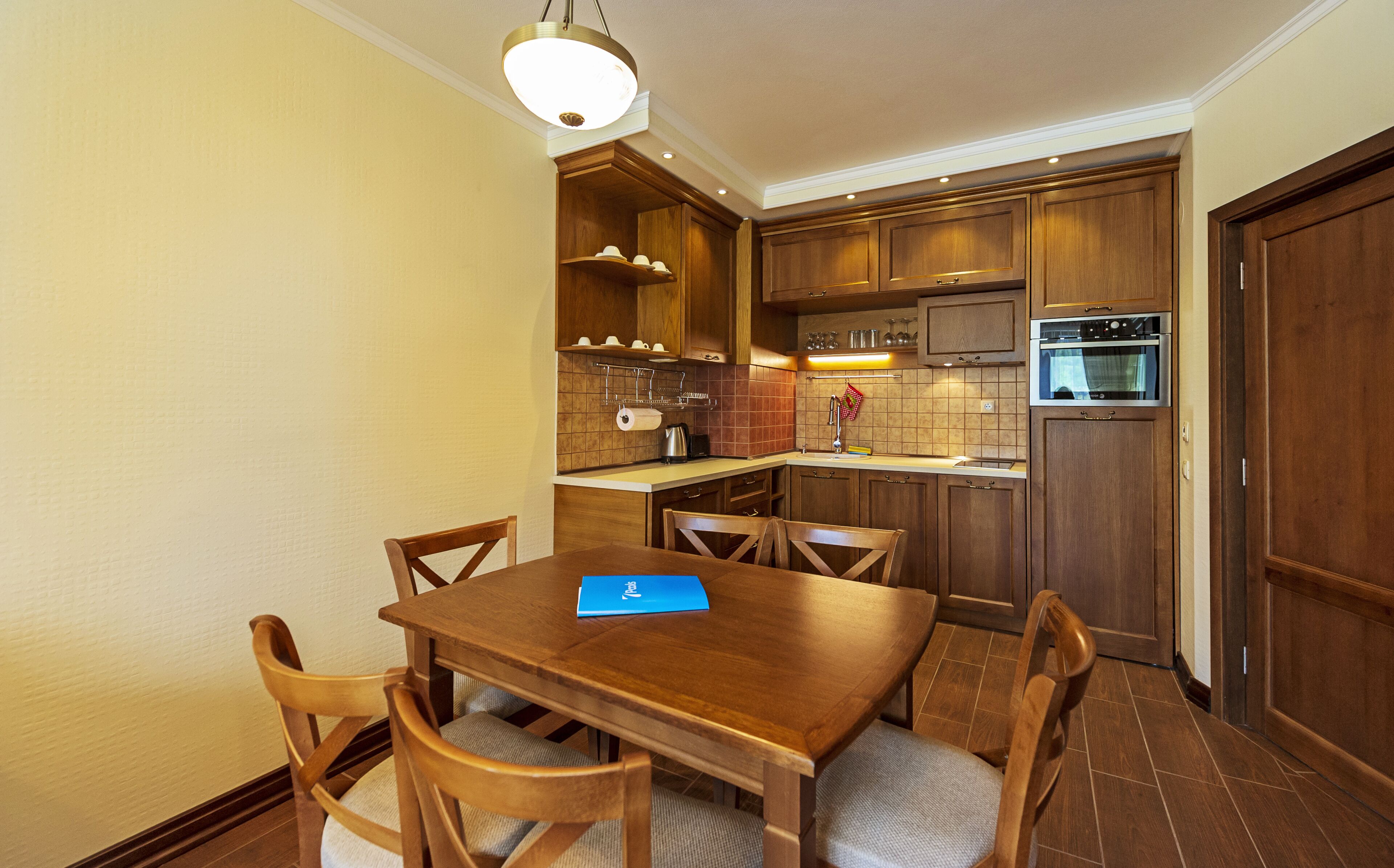 A compact kitchen with wooden cabinets, a dining table with chairs, and a built-in oven.
