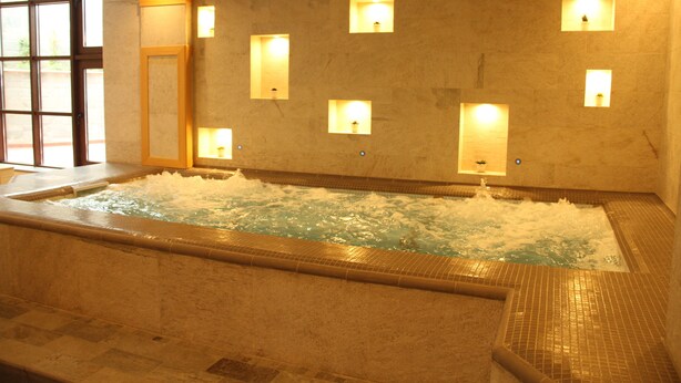 Un jacuzzi con múltiples luces empotradas en la pared, suelo de baldosas y vistas al exterior a través de un ventanal grande.