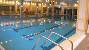 Una piscina interior con varias pistas, sillas de descanso y una zona de estar con una silla roja.