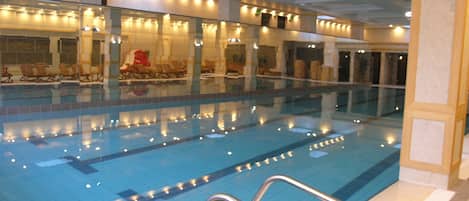 Une piscine intérieure dotée de plusieurs couloirs de nage, de chaises longues et d’un espace détente avec un fauteuil rouge.