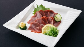 Une assiette rectangulaire blanche, garnie de fines tranches de viande rouge, d’une tranche de concombre, d’un quartier de citron et de quelques herbes vertes.