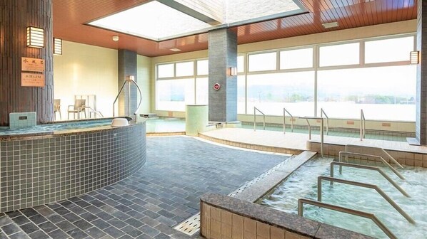 Un área de spa con un jacuzzi, una piscina y una sala iluminada con vistas.