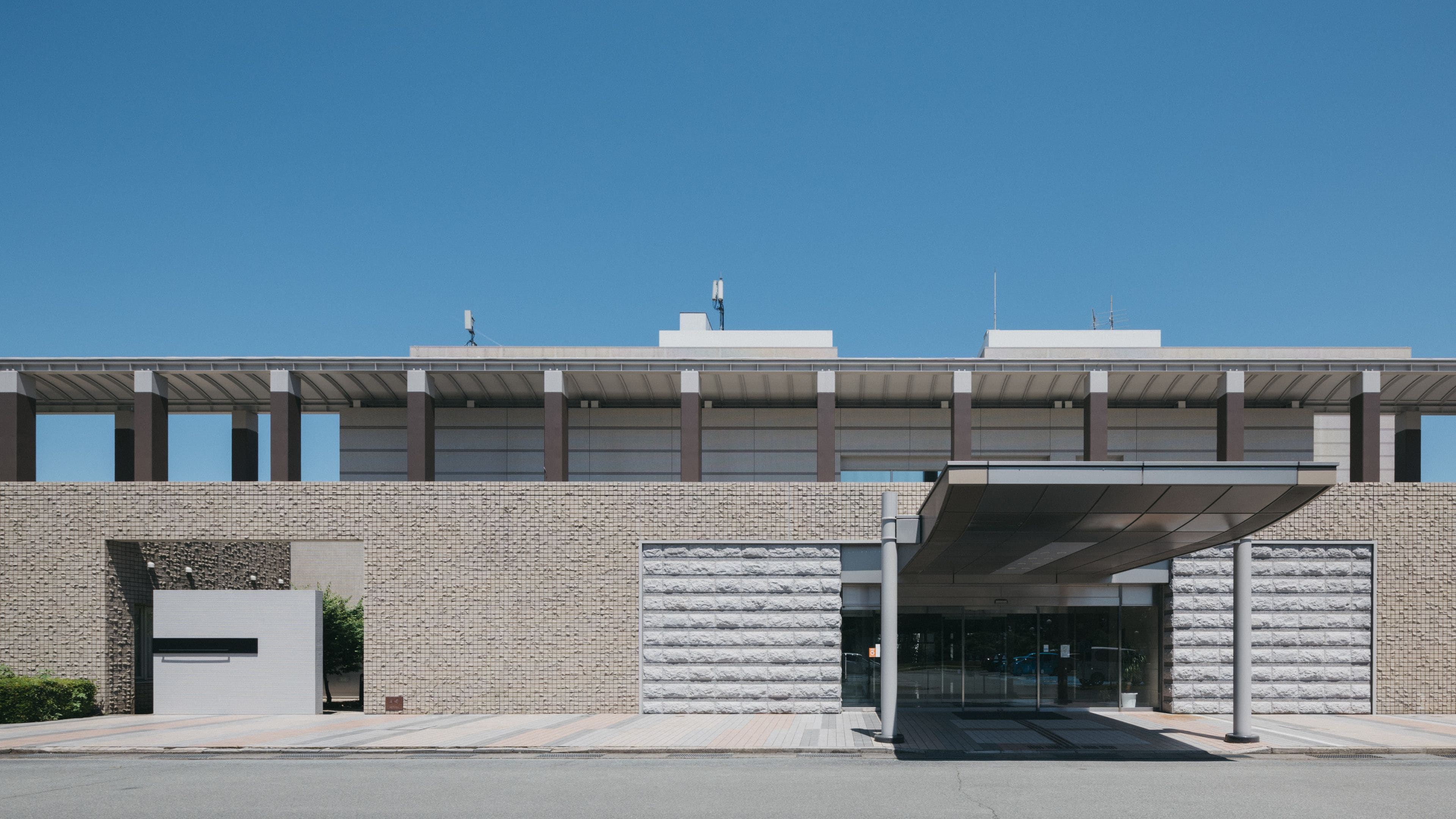A modern building with a flat roof, large windows, and a covered entrance.