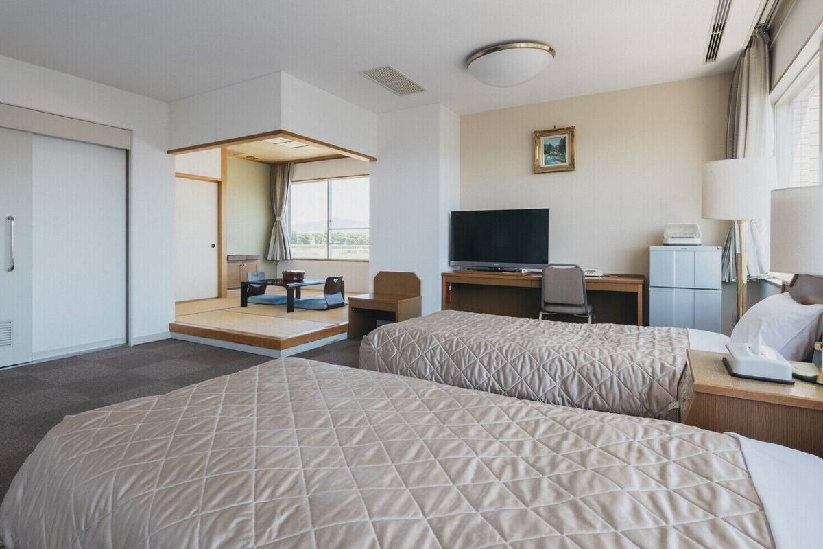A hotel room with two beds, a desk with a TV, a chair, a lamp, and a window with a view.