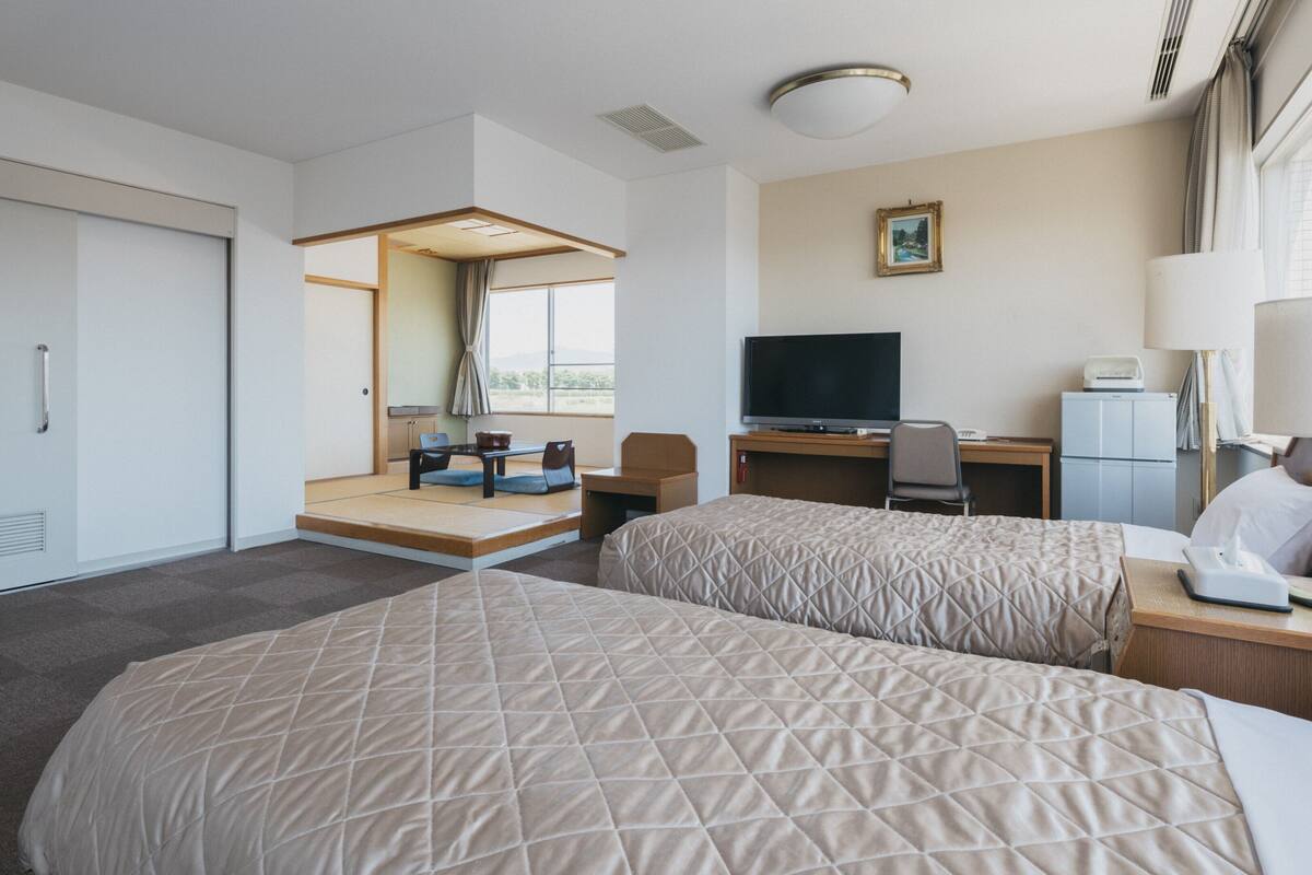 A hotel room with two beds, a desk with a computer, a television, and a small refrigerator.