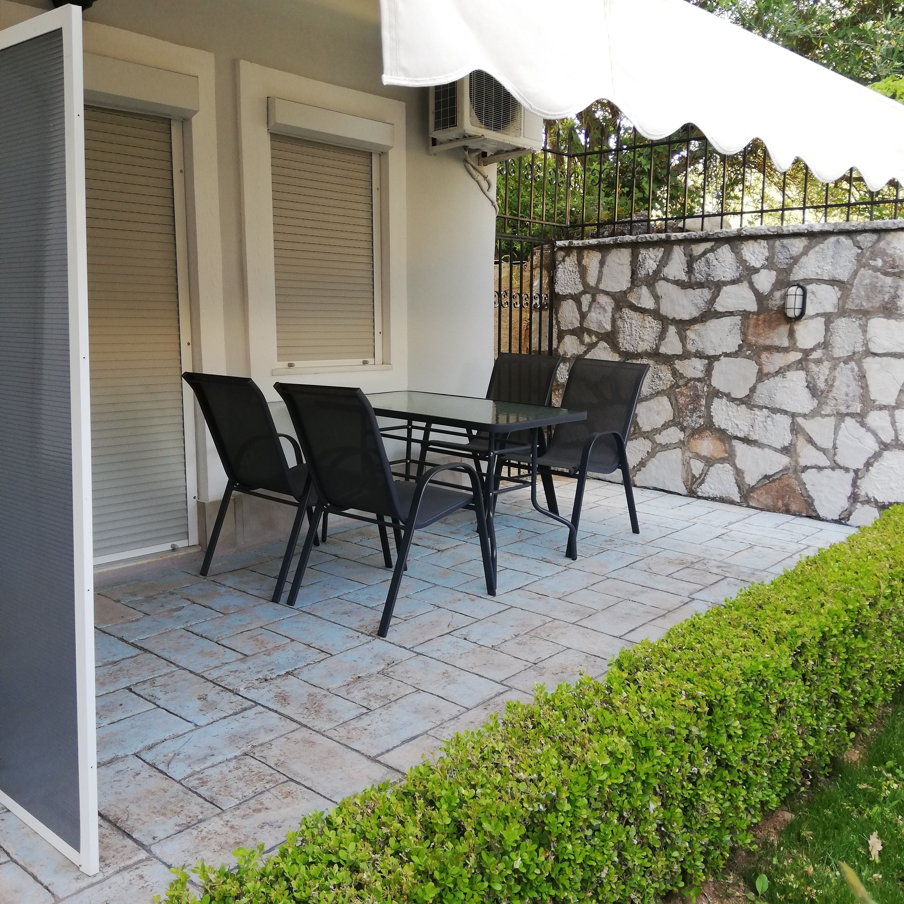 A patio with a table and chairs, a stone wall, and a hedge.
