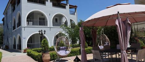 A two-story building with a balcony, outdoor seating area with chairs and tables, and a clear sky.