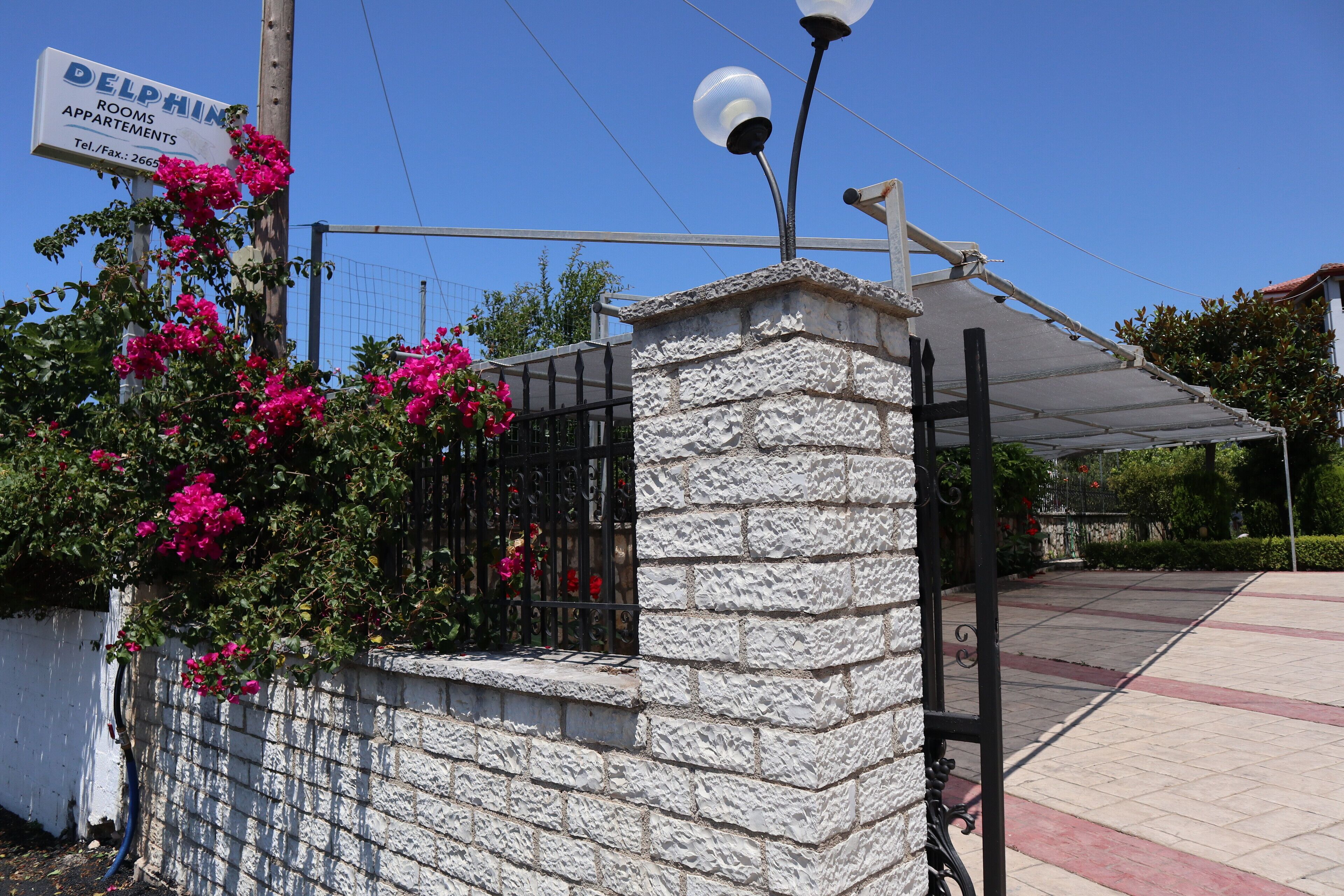Un muro de piedra con una reja de metal, un cartel que dice 'Delphin Apartments' y una farola.