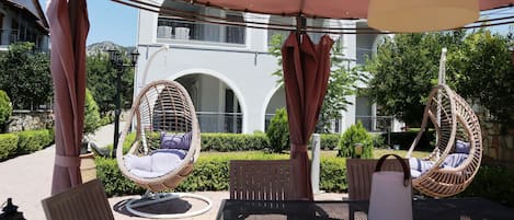 Un patio con sillas de mimbre, una mesa, una sombrilla y un edificio al fondo.