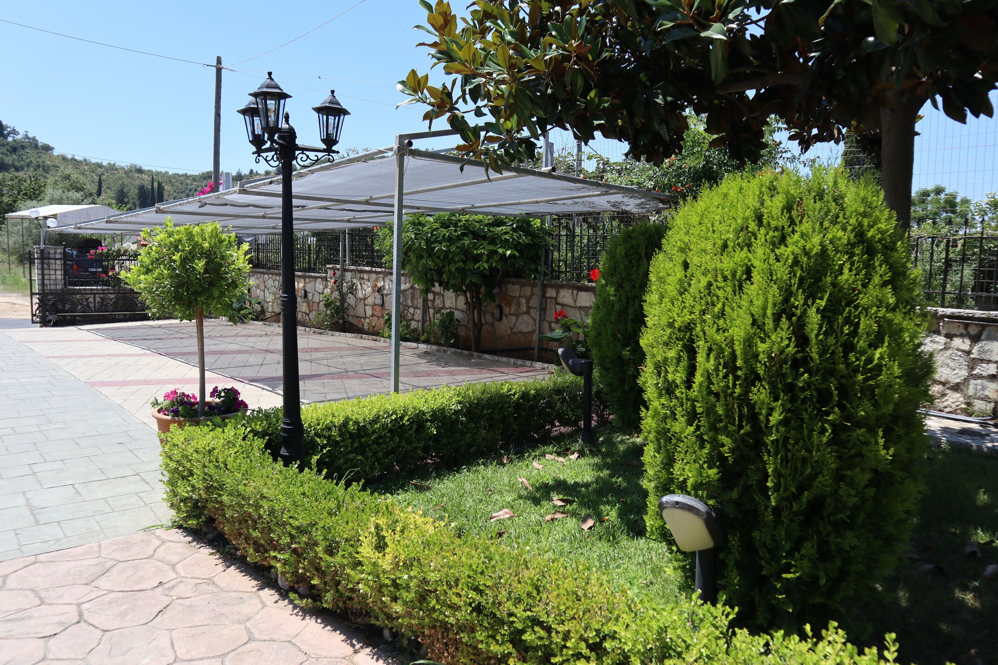Un jardín con pérgola, muro de piedra y setos cuidados.