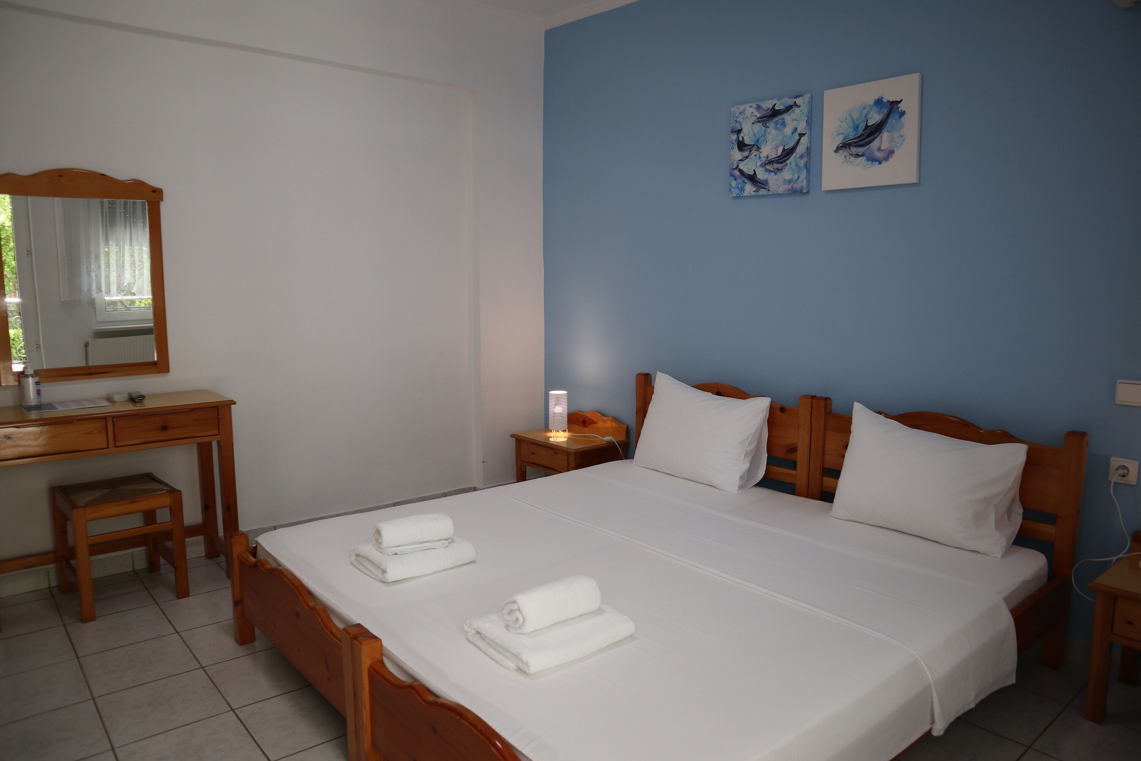 A bedroom with a wooden bed, white linens, a wooden desk, a nightstand, and a mirror.