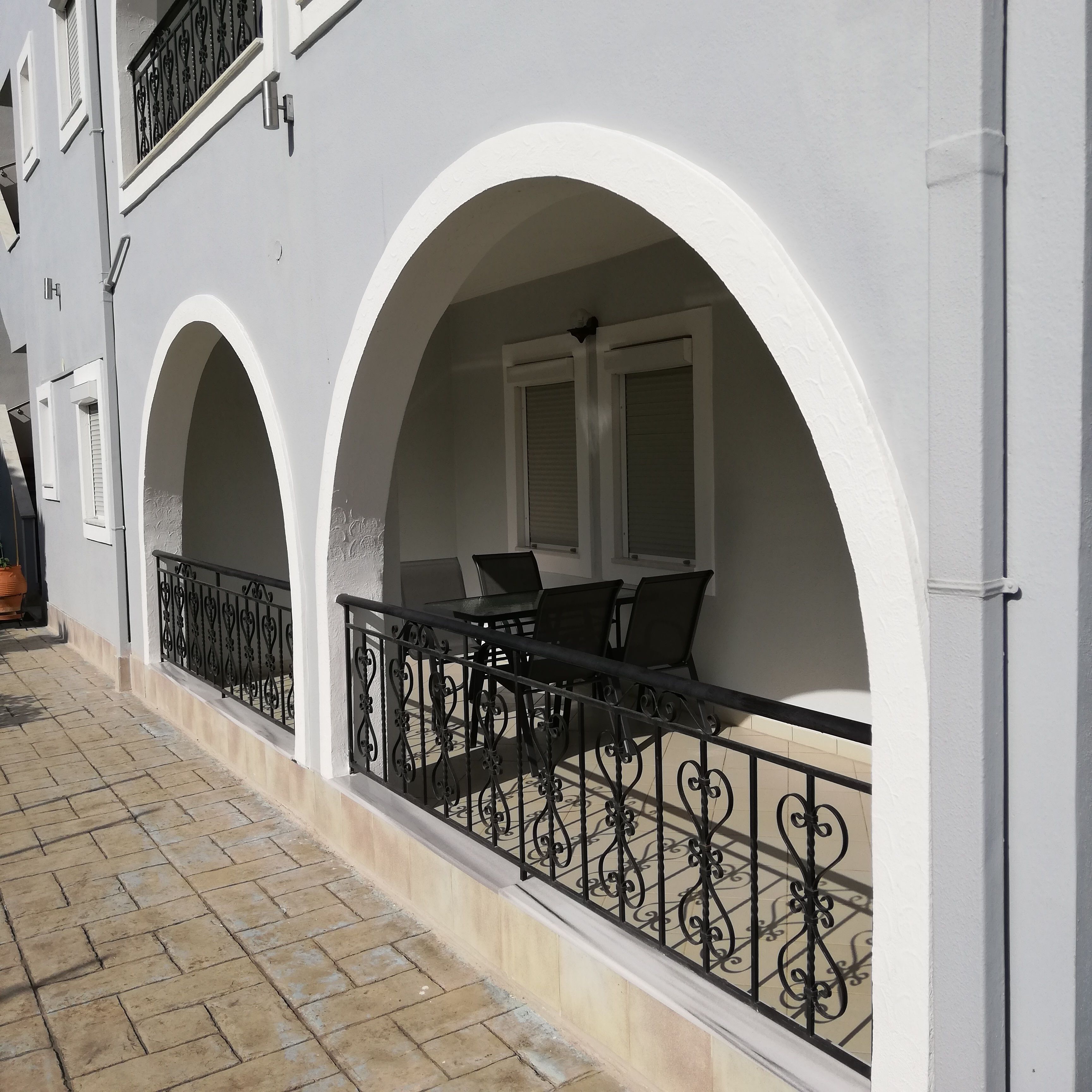 A building with white exterior walls, two balconies with black wrought iron railings, and a tiled floor.