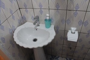 A bathroom with a white sink, a faucet, a soap dispenser, and a toilet paper holder. - Elu Hotel Appart (Douala)