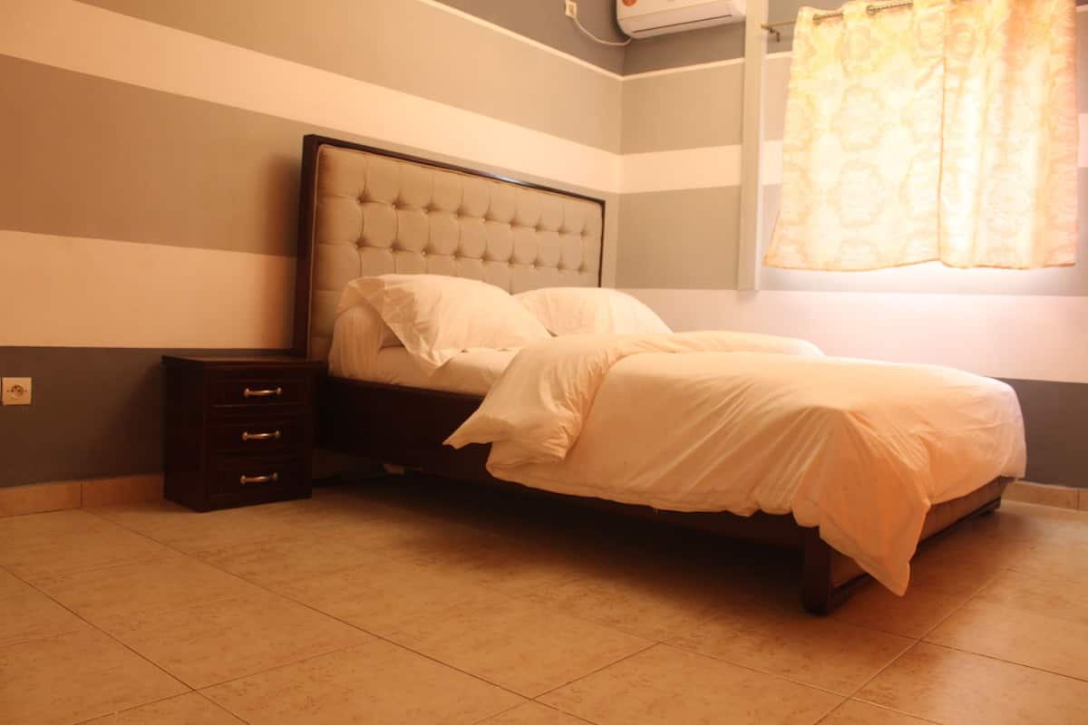 Un dormitorio con cama, mesita de noche y ventana con cortinas.