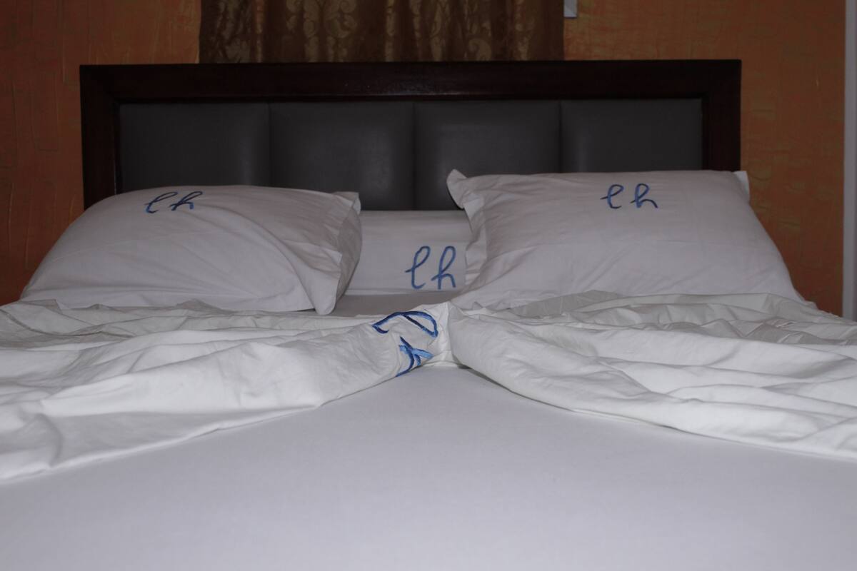 Una cama con sábanas y almohadas blancas con iniciales.