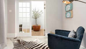 Una habitación con un sillón azul, un felpudo con estampado de cebra, una planta en maceta y una puerta que da al exterior.