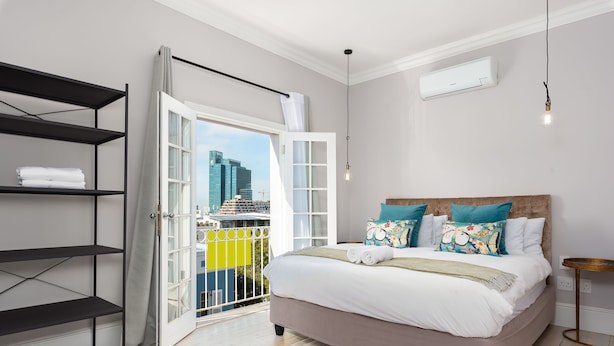Un dormitorio con cama, una alfombra gris, una puerta blanca que da a un balcón y un estante negro.