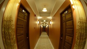 Un pasillo de hotel con puertas de madera, letreros numerados de habitaciones y alfombra estampada.