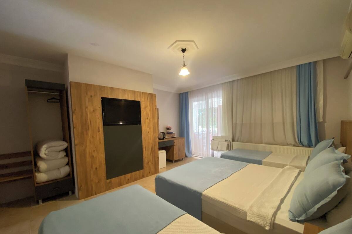 A hotel room with two beds, a wooden wardrobe, a desk, and a window with curtains.