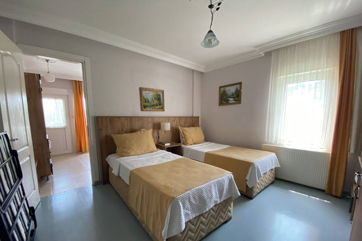 A hotel room with two beds, a wooden headboard, a small bedside table with a lamp, and two paintings on the wall.