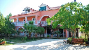 A multi-story building with balconies, a paved courtyard, and surrounding greenery. - Villasabella (Zakynthos)