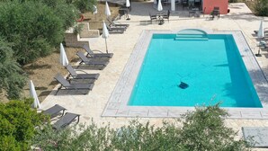 A swimming pool with lounge chairs and umbrellas, surrounded by greenery and a building with a red roof. - Villasabella (Zakynthos)