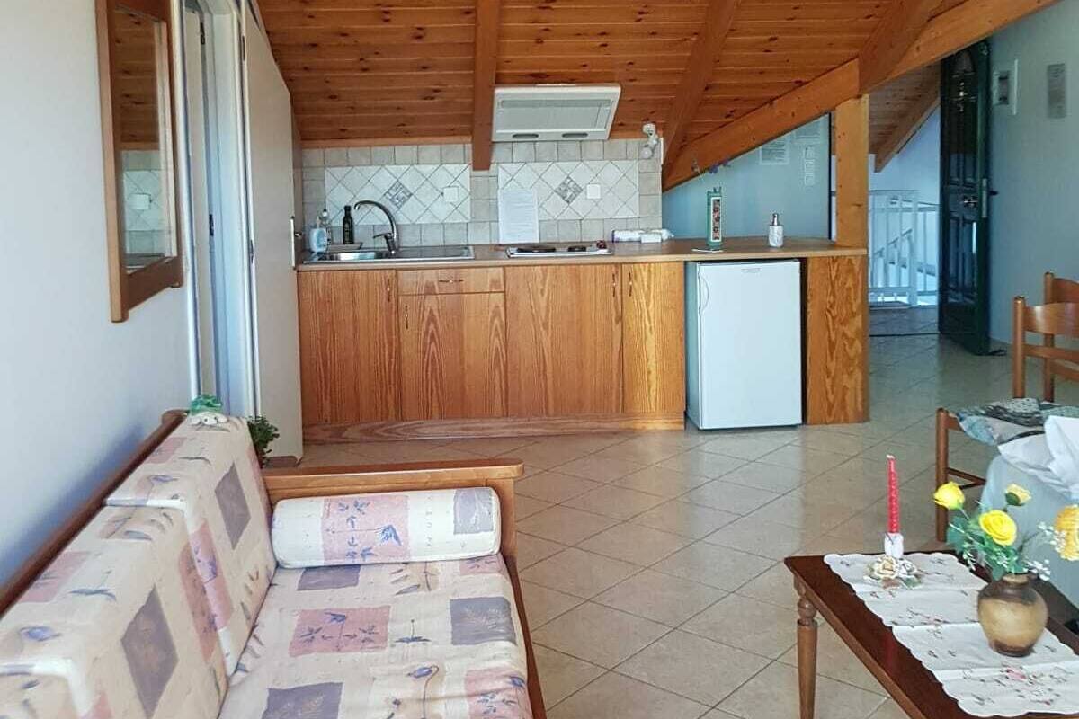 A cozy wooden interior with a sofa, a dining table with a vase, and a kitchen area with a refrigerator and sink.