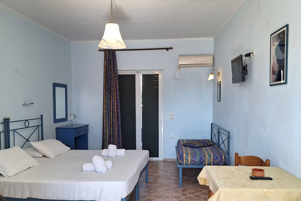 A hotel room with two beds, a small table, a chair, a desk, a lamp, a mirror, and a door.