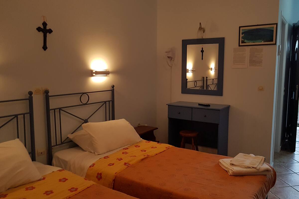 A hotel room with two beds, a desk, a mirror, and a cross on the wall.