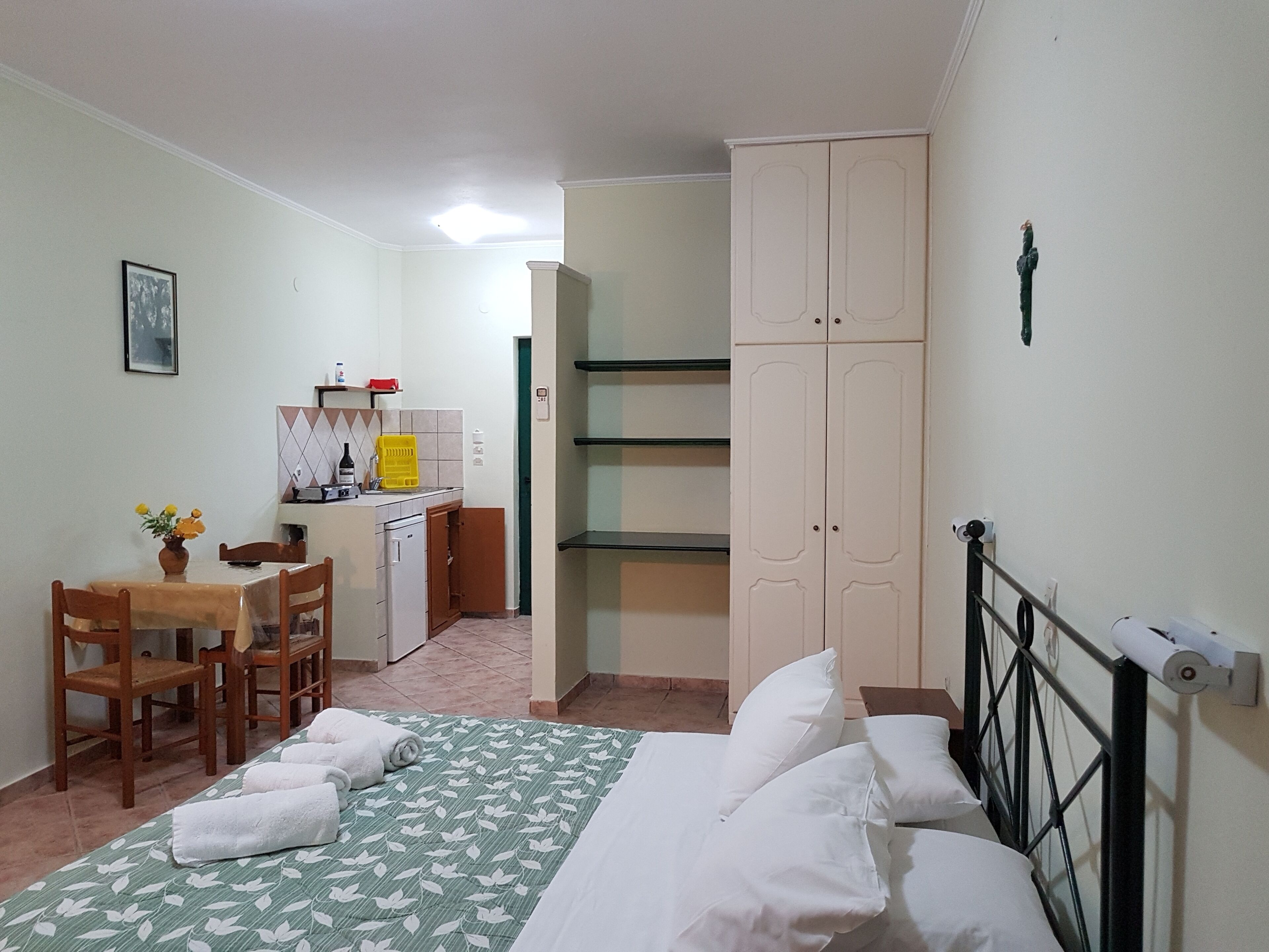 Une chambre comprenant un lit, un bureau avec des chaises, un coin cuisine et une armoire.