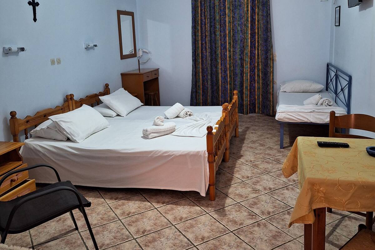 A bedroom with two beds, a desk, a chair, a table, and a hanging light fixture.